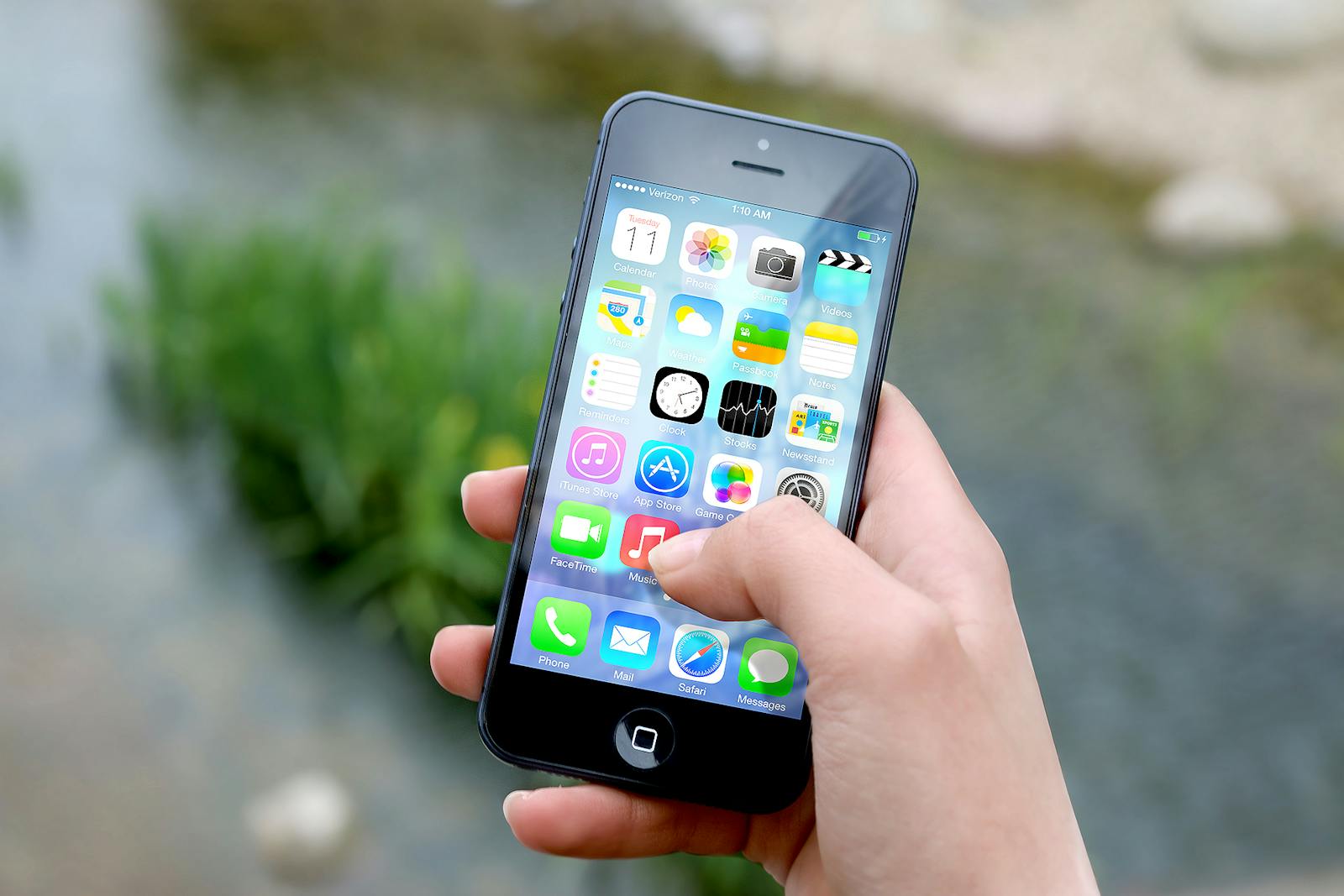 Close-up of a hand holding a smartphone outdoors near a river.