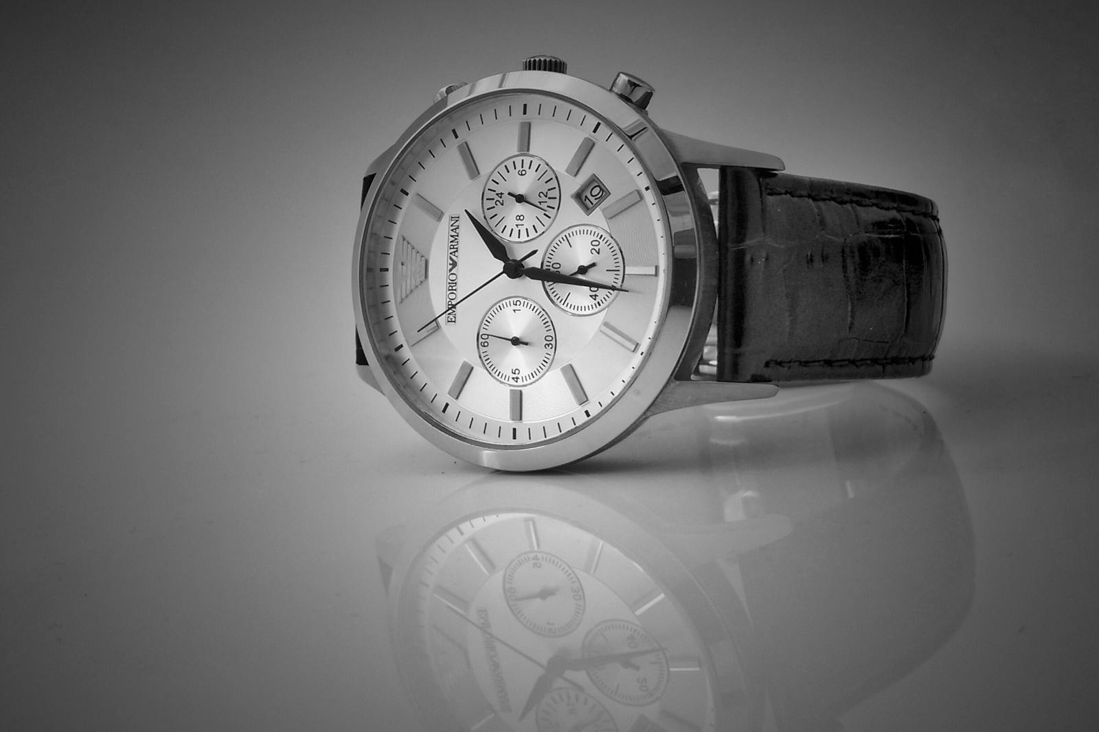 Elegant black and white close-up of a luxury wristwatch with a reflective stainless steel body and leather strap.